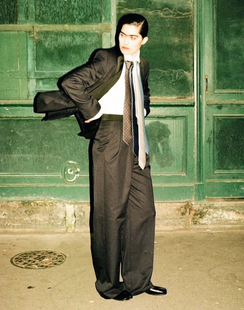 Stylish adult male in oversized suit stands against a green door, bathed in moody lighting, showcasing a blend of fashion and urban style.
