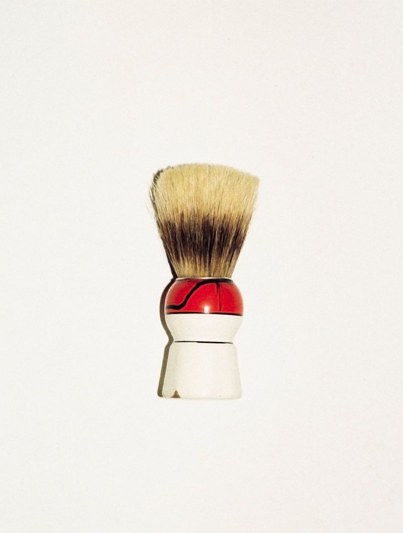 Close-up of a shaving brush with a white and red handle against a clean white background, showcasing textures and minimalist composition.