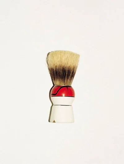 Close-up product shot of a traditional shaving brush with white and red handle against a plain background