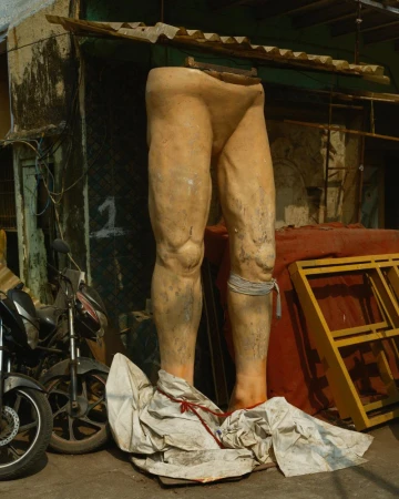 Outdoor shot of a weathered, headless statue of legs, propped up by a building, with motorcycles parked nearby, creating an urban scene.
