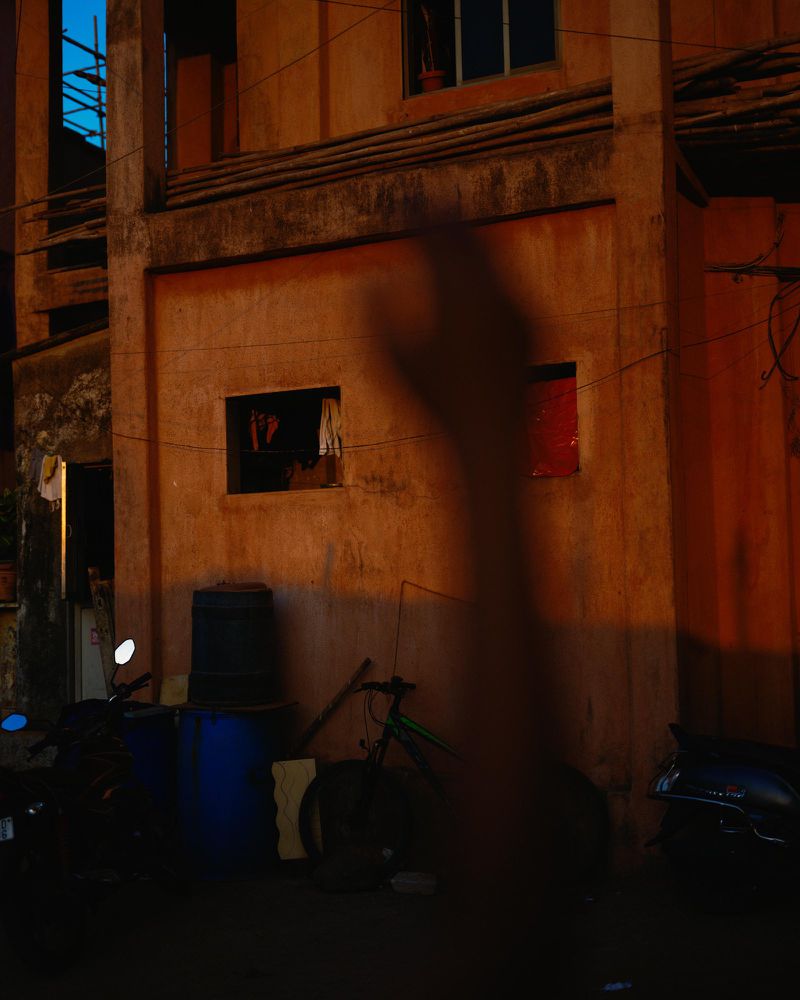Exterior of a building with closed windows and doors, a motorcycle, a bike, and a large hand shadow in front of it at night.