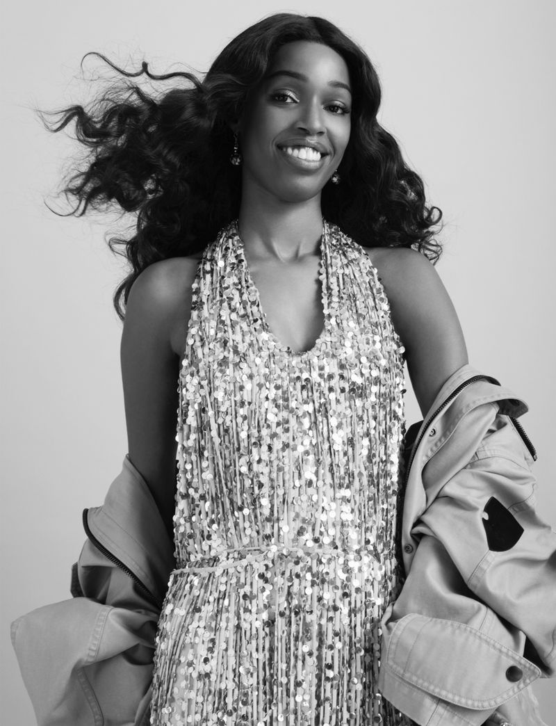 Black and white portrait of a smiling Black woman in a sequin dress with a jacket, set against a neutral background.