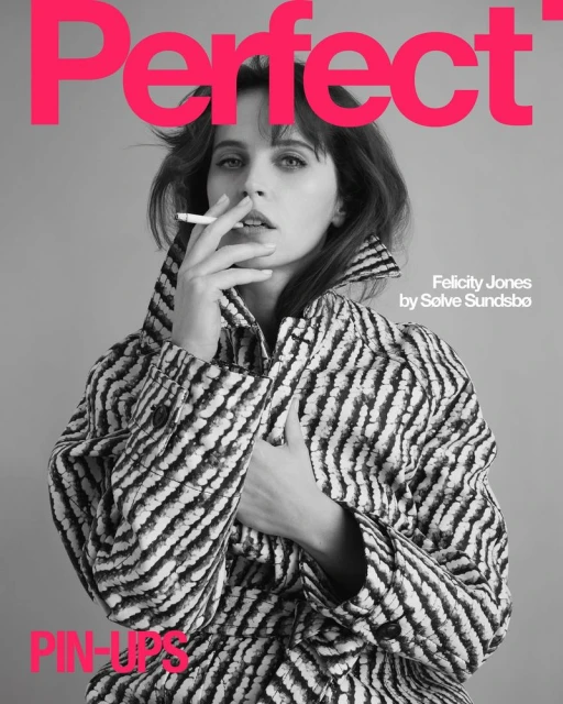 Black and white magazine cover featuring Felicity Jones in a patterned coat, holding a cigarette, against a grey backdrop.