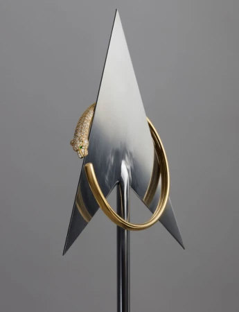 A golden panther sculpture with green eyes wraps around a metal hoop with a triangular metal design, standing on a sleek metal stand.