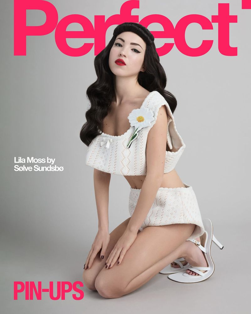 Woman in a white knit bikini and heels poses on her knees, featured on the cover of Perfect magazine in a photo studio.