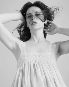 Monochrome portrait of a woman with windblown hair wearing a lace-trimmed strap top against a seamless white background.