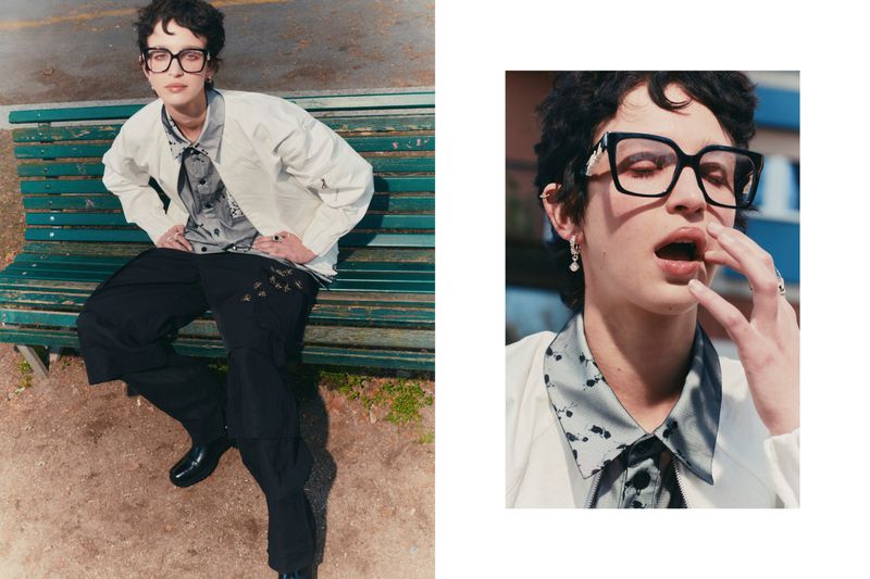 A woman in glasses sits on a bench in daylight, wearing a white jacket and black pants, near a building. Close up of her face on right.