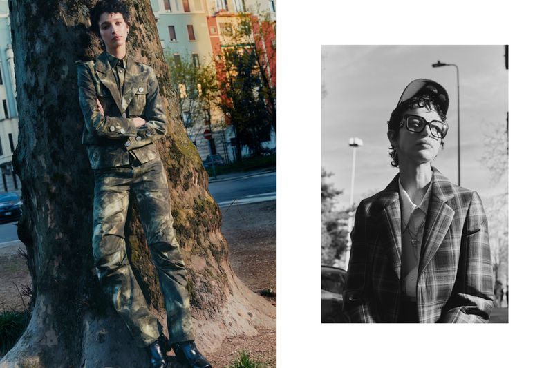Fashionable person in a camouflage suit leans against a tree in an outdoor setting; a black and white portrait adds contrast.