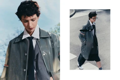 Model wearing a grey coat over a white shirt and dark tie with short dark hair in an outdoor setting