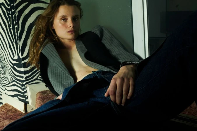 Adult female in blazer poses indoors against zebra print wall. She wears jeans in portrait shot with dark mood lighting.