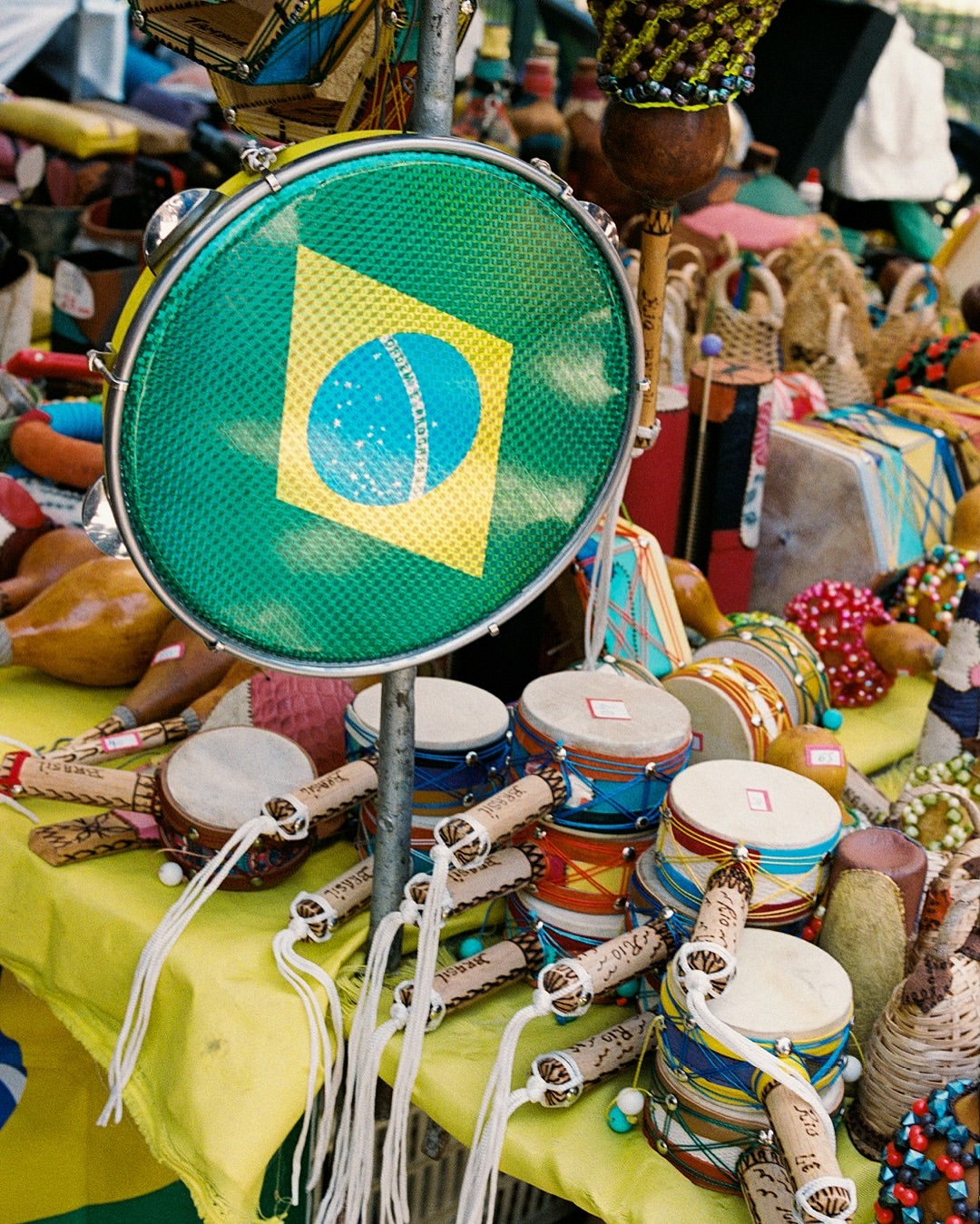 Overhead shot of Brazilian percussion instruments, including tamborims, arranged on a yellow cloth-covered table.