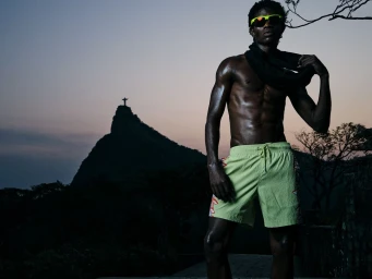 Man wearing neon shorts and sunglasses with the Christ the Redeemer statue visible in the distant background.