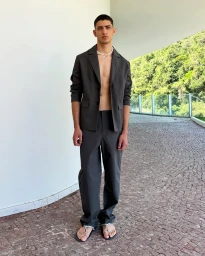 Man wearing a dark grey suit jacket and trousers with sandals standing outdoors on stone paving