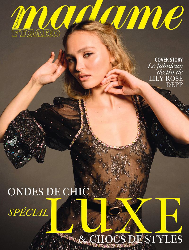 Lily-Rose Depp features on a magazine cover with bold text. She is wearing a black lace dress and posing with her hands raised.