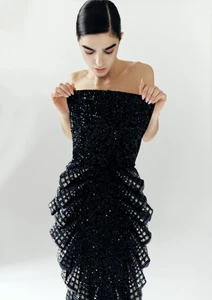 Model in strapless black sequin evening dress looking down against a bright white background for Vogue Arabia
