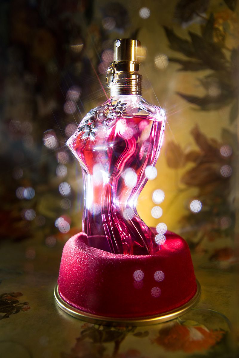 Elegant perfume bottle stands on a velvet cushion against a bokeh background in a close-up studio shot with warm, inviting lighting.