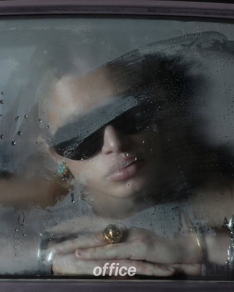 Close-up studio shot of a model wearing sunglasses and jewelry behind a steamy window with water droplets creating a unique texture.