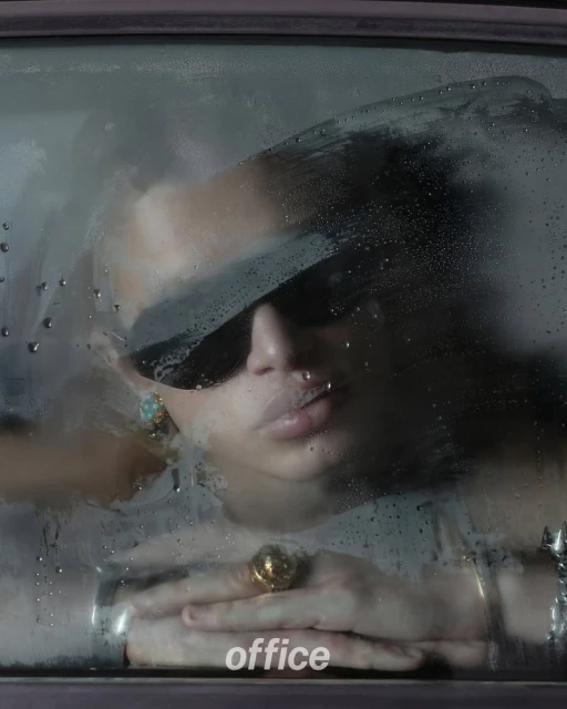Close-up studio shot of a model wearing sunglasses and jewelry behind a steamy window with water droplets creating a unique texture.