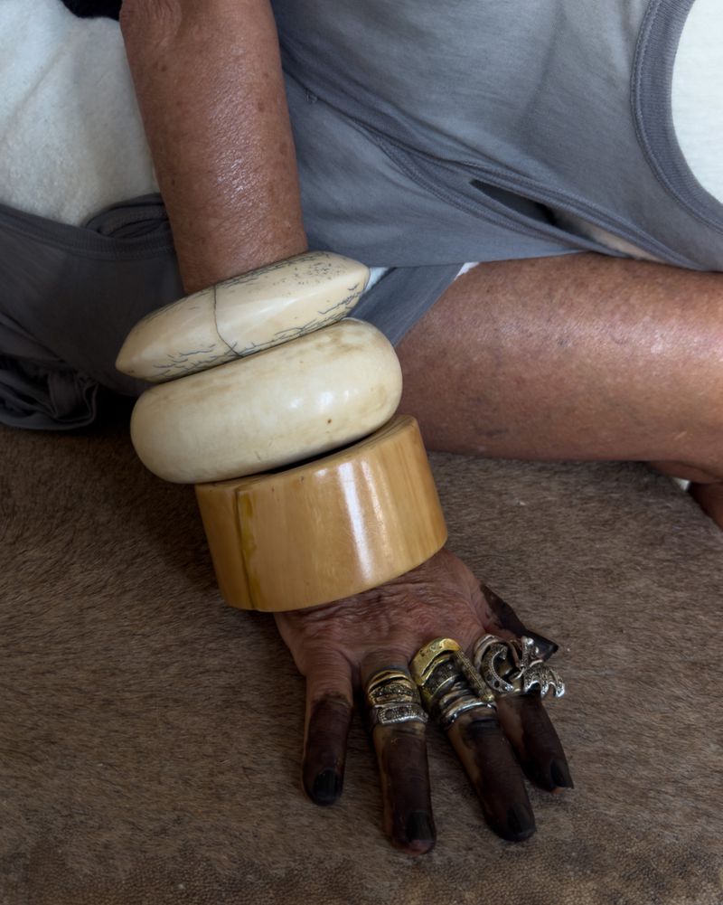 Close-up of a person's hand and arm adorned with a collection of chunky bangles and various rings, set against a blurred background.