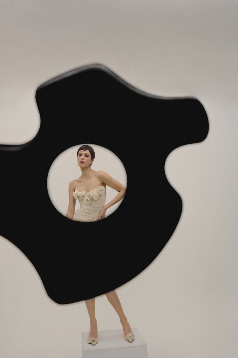 A woman poses in a floral dress in a photo studio, framed by a black abstract shape, showcasing fashion photography.