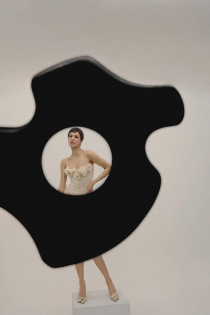 A woman poses in a floral dress in a photo studio, framed by a black abstract shape, showcasing fashion photography.