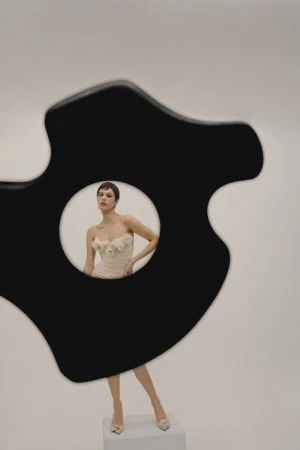 A woman poses in a floral dress in a photo studio, framed by a black abstract shape, showcasing fashion photography.