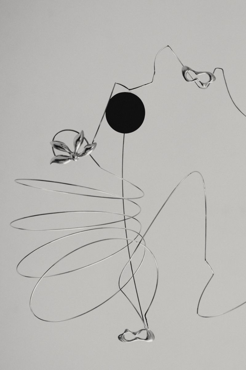 Abstract mobile sculpture with silver wire, a black circle, and amorphous forms against a plain gray background, artful composition.