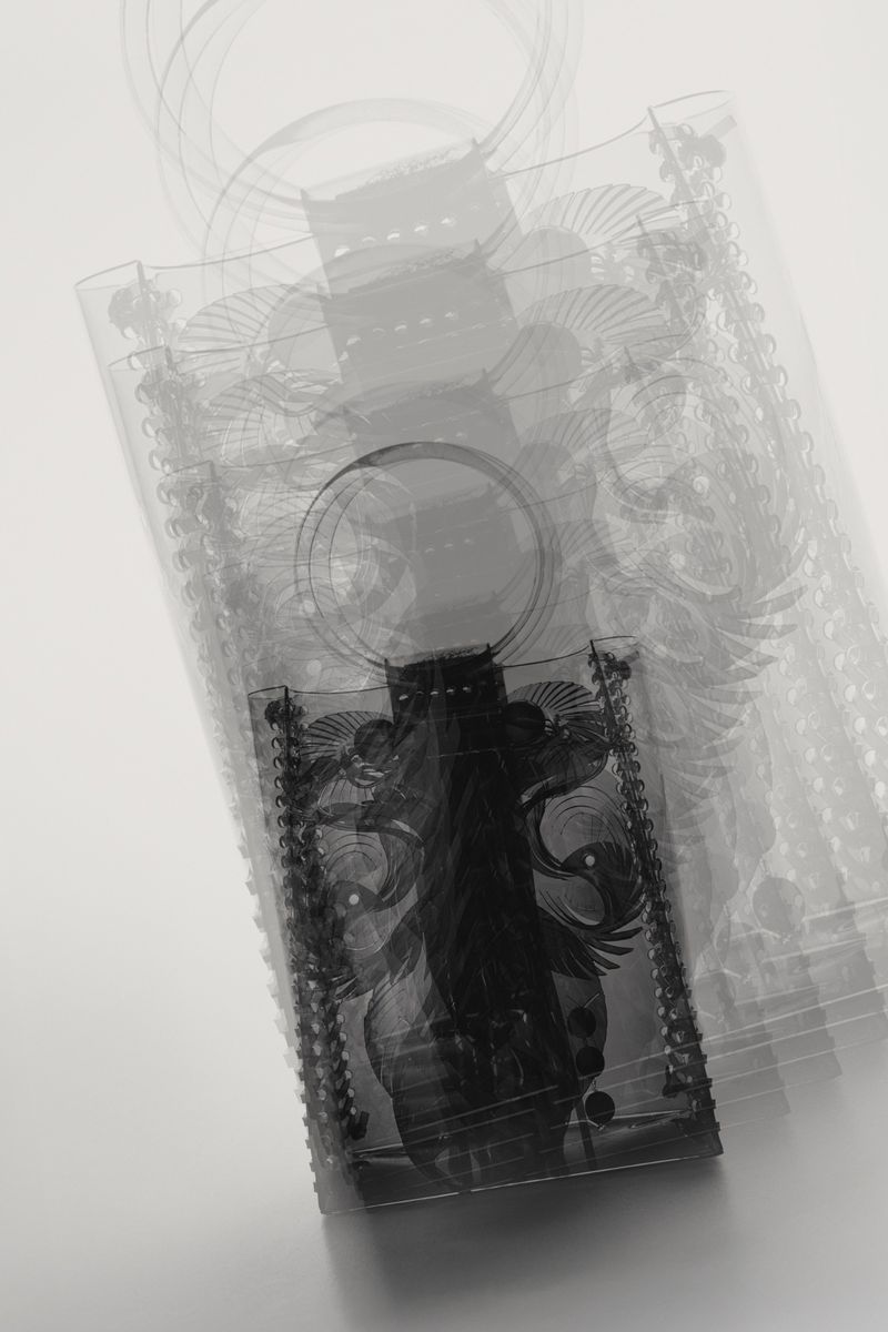 Ghosted effect of multiple semi-transparent tote bags overlapping. Black and white tones with an ornate dark rectangle design in the middle.