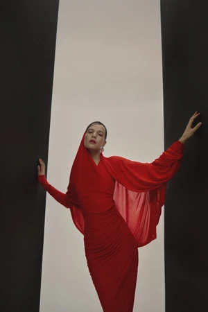 Model in a bright red dress posing against a central white vertical panel framed by dark side pillars