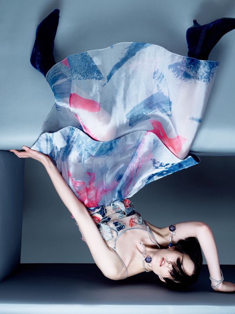 Woman posing with abstract painted dress and jewelry in a studio with geometric background. Fashion editorial photography.