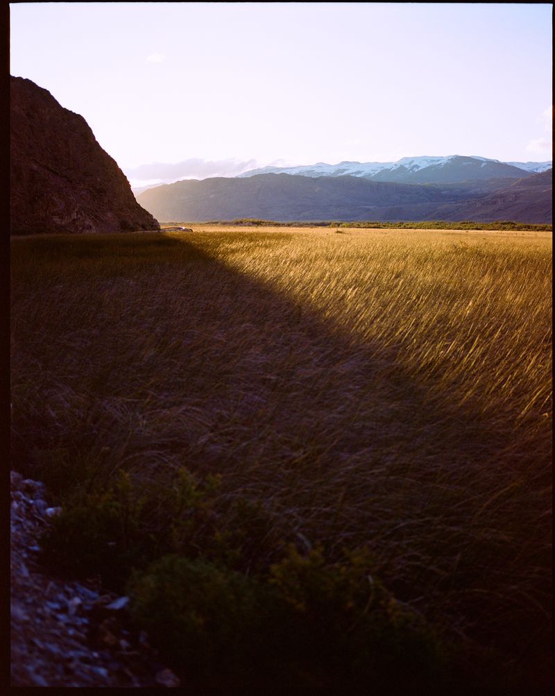 Landscape view of a grassy field with mountains in the distance under a bright sky with a shadow cast across the field.