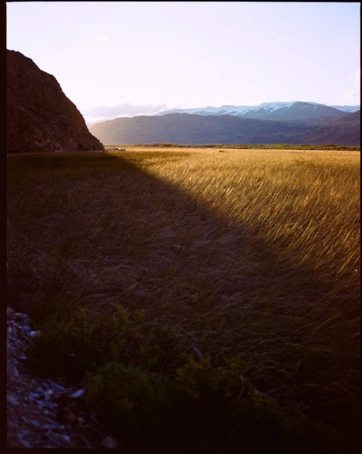 Landscape view of a grassy field with mountains in the distance under a bright sky with a shadow cast across the field.