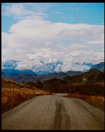 Scenic road leads to snow-covered mountains under a partly cloudy sky, highlighting natural beauty and a sense of adventure in a remote area.