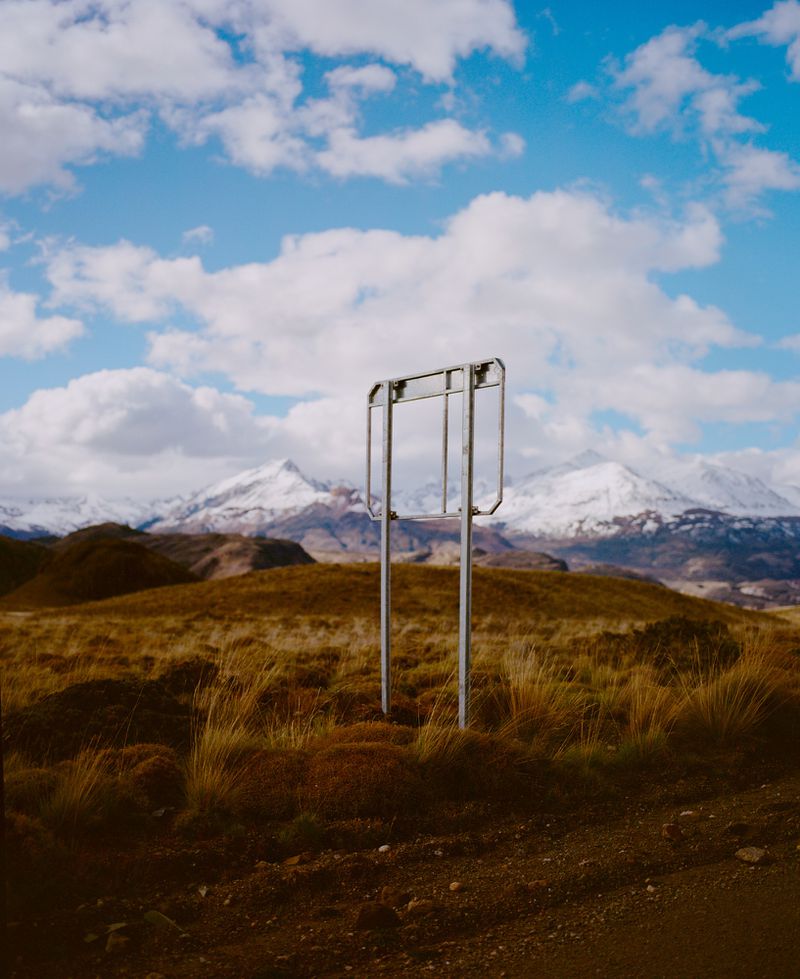 Metal frame structure in rural landscape with snow-capped mountains under a bright cloudy sky in daylight, creating a natural background.