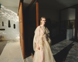 Model wearing a sheer cream tulle gown standing near large wooden doors in a sunlit architectural interior for Grazia Germany.