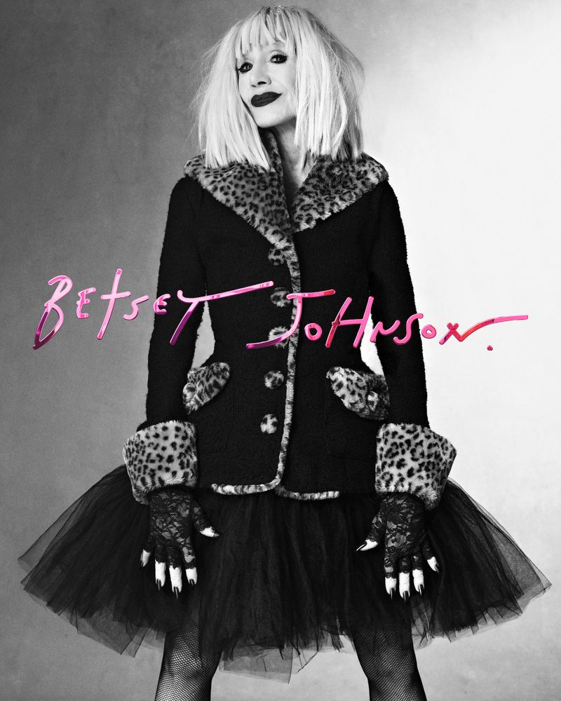 Woman in black coat with leopard print trim and black tulle skirt posing in a photo studio for Betsey Johnson campaign.