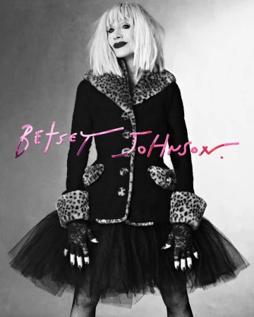 Woman in black coat with leopard print trim and black tulle skirt posing in a photo studio for Betsey Johnson campaign.
