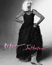 Woman in black textured dress with mesh sleeves and sparkly boots laughing against a gradient studio background