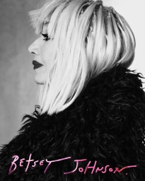 Profile portrait of a blonde woman wearing a textured dark coat against a plain background for Betsey Johnson.