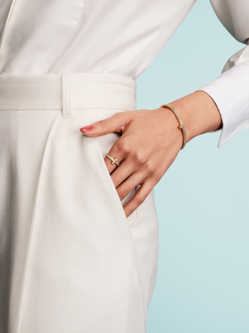 Close-up of a woman's hand with a diamond ring and bracelet, set against a light blue background, showing jewelry and elegant fashion.