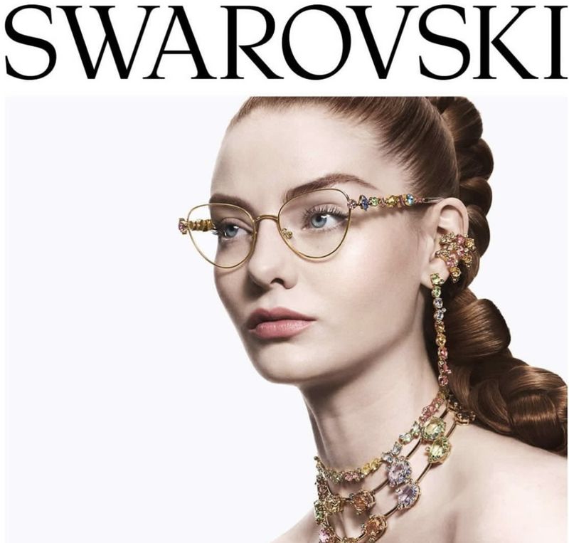 Glamorous studio shot: Elegant adult woman with gold-framed glasses and ornate jewelry. White backdrop emphasizes the subject's radiant beauty.