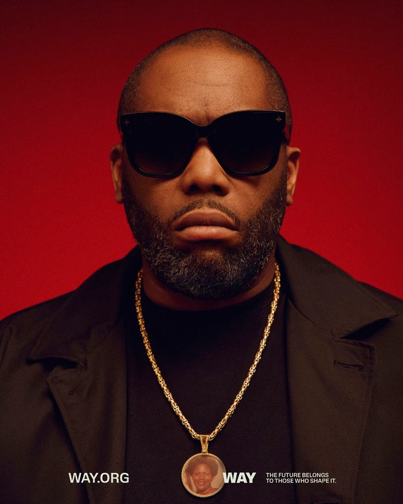 Close-up portrait of a Black man with sunglasses and gold chain necklace against a solid red background for WAY Campaign.