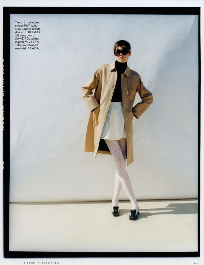 Model in a tan coat and black sunglasses standing against a white seamless background with text overlay on the left margin