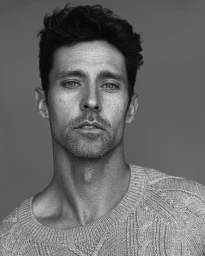 Black and white portrait of a man in a textured knit sweater against a plain dark background.