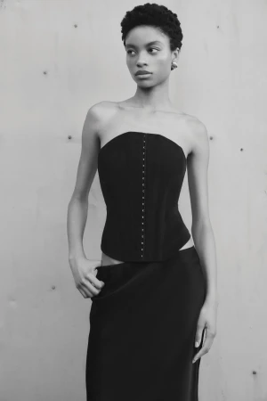 Monochrome portrait of a Black female model in a black corset and skirt against a grey studio backdrop, demonstrating fashion and style.