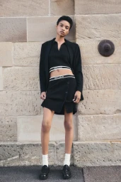 Model in a black matching top and skirt leaning against a large stone masonry wall outdoors