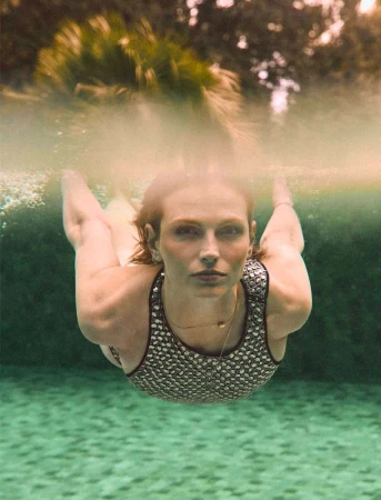 Underwater view of a woman with red hair wearing a patterned swimsuit. Bubbles and a blurred green background are visible.