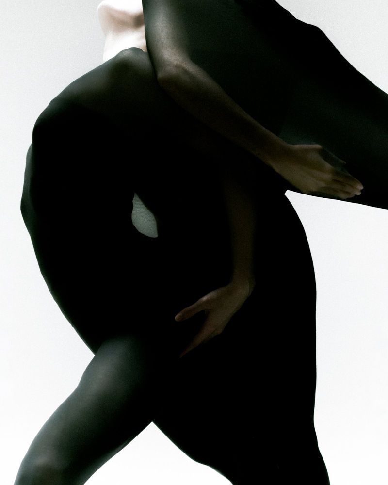 Monochromatic fashion shot featuring two women covered in black fabric posing against a stark white backdrop in a studio setting.