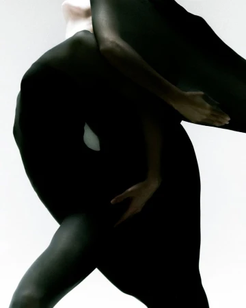 Monochromatic fashion shot featuring two women covered in black fabric posing against a stark white backdrop in a studio setting.
