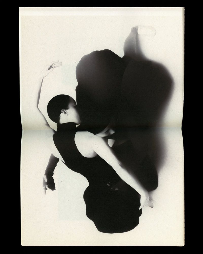 Black-and-white photograph features a woman in a dark dress striking a ballet pose against a light backdrop with a distinct shadow.